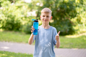 Smiling boy holding sports water bottle and showing thumbs up outdoors on sunny day