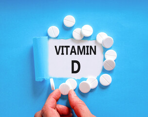 Vitamin D symbol. Concept words Vitamin D on beautiful white paper. White pills tablets. Doctor's hand. Beautiful blue background. Medical healthy lifestyle Vitamin D concept.