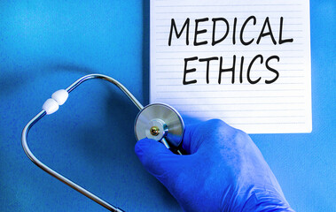 Medical ethics symbol. Concept words Medical ethics on beautiful white note. Doctor's hand in blue glove. Stethoscope. Beautiful blue background. Medical healthy lifestyle medical ethics concept.