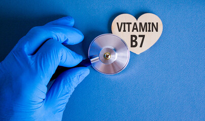 Vitamin B7 biotin symbol. Concept words Vitamin B7 on beautiful wooden heart. Doctor's hand in blue medical glove. Stethoscope. Beautiful blue background. Medical healthy lifestyle Vitamin B7 concept.