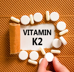 Vitamin K2 phylloquinone symbol. Concept words Vitamin K2 on beautiful white paper. White pills. Doctor's hand. Beautiful brown background. Medical healthy lifestyle Vitamin K2 phylloquinone concept.