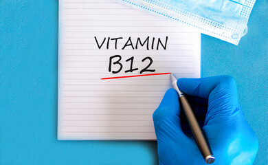 Vitamin B12 symbol. Concept words Vitamin B12 on beautiful white note. Doctor's hand in blue medical glove. Medical mask. Beautiful blue background. Medical healthy lifestyle Vitamin B12 concept.