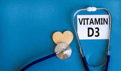 Vitamin D3 symbol. Concept words Vitamin D3 on beautiful white card. Wooden heart and stethoscope. Beautiful blue background. Medical healthy lifestyle Vitamin D3 concept.