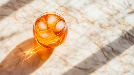 Aperol Spritz top view: vibrant orange drink with ice cubes in round glass on white marble with golden veins and soft shadows - minimalist summer refreshment theme.