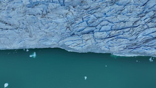 Aerial view of the stark contrast between the textured, icy glacier and the smooth, turquoise water dotted with icebergs, Chile.