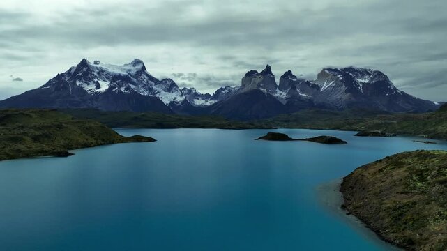 Aerial view of the majestic Torres del Paine mountains reflected in the turquoise waters of the lake, contrasting with the green vegetation, Chile.