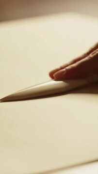 Creating a Sharp Crease: Hand uses a bone folder tool on premium paper for a clean, crisp fold&mdash;perfect for crafting, bookbinding, & professional documents.
