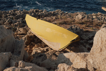 Old yellow canoe fragment on rocky seashore with blue sea in background