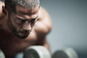 young man with tense neck strains while lifting dumbbells in gym setting