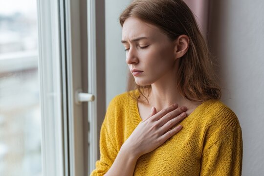 Young Woman Struggling with Breathing Issues by the Window in a Cozy Indoor Setting