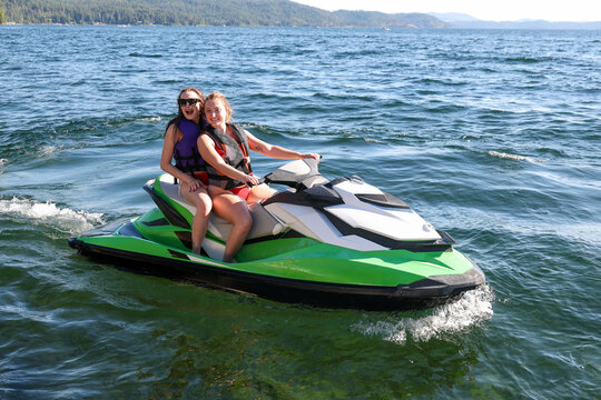 Two young women having fun on Couer D'Alene lake in Idaho riding the water on a fast jet ski watercraft outside on a long summer day. The sisters are laughing and enjoying the family time together. 