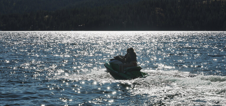 Two young women having fun on Couer D'Alene lake in Idaho riding the water on a fast jet ski watercraft outside on a long summer day. The sisters are laughing and enjoying the family time together. 