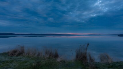 Obraz premium Serene Lake Scene Featuring Calm Water, Grass, and a Dramatic Sky