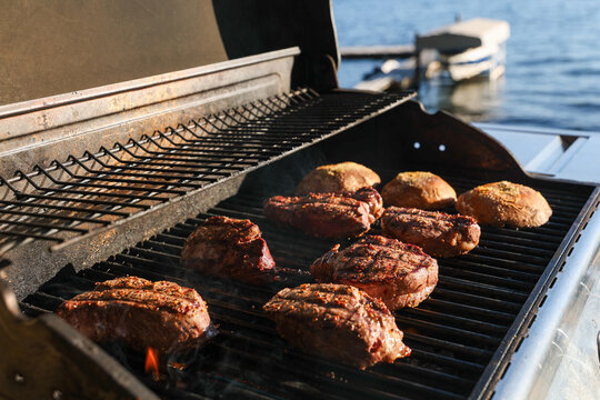 Grilling prime fliet mignon steaks and portabella mushrooms on a bbq grill outside on a lakeside vacation home.
