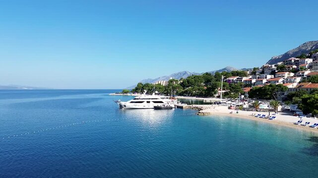 4K Forward Drone Flight Over Brela Beach on a Bright Sunny Day, Revealing Turquoise Adriatic Sea, Mountain Backdrop, and Yacht Along the Croatian Coast