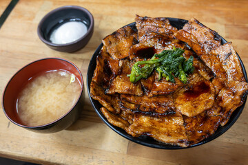 A delicious Buta Don bowl featuring grilled pork slices glazed with a savory sauce, served on steamed rice, miso soup, and greens with a side of poached eggs