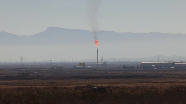 An industrial facility in Iran with a torch burning associated gases, Against the backdrop of mountains. fire on Iranian oil refinery and smoking in the air, factory hidden underground. slow motion.