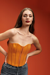 Young beautiful woman poses confidently in vibrant orange corset top against bold background