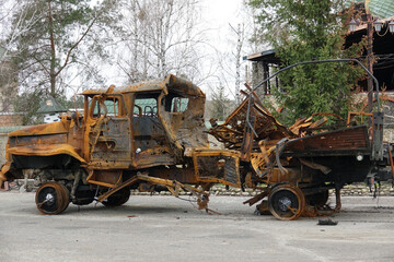 Burnt destroyed military style truck with heavily rusted frame and missing wheels standing on an empty road showing severe fire damage and structural destruction in an outdoor urban environment