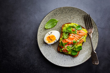 Toast with avocado cream and smoked salmon over black background, top view