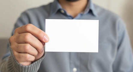 A close-up, eye-level shot focusing on a person's hand, wearing a grey knitted sweater, holding up a blank, rectangular white card