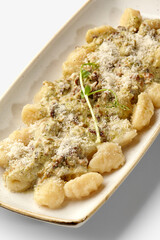 Potato gnocchi with pesto sauce, walnuts and parmesan resting on a white plate