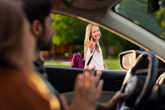 Start of school year. Parents bringing their daughter to school, sitting in car and waving goodbye to child girl, view from inside automobile