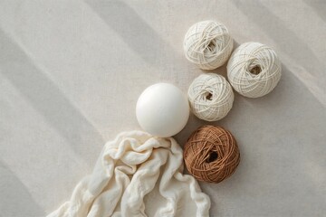A minimalist flat lay of natural fiber yarn balls and a white sphere on a soft, textured fabric, representing organic crafting and simplicity.