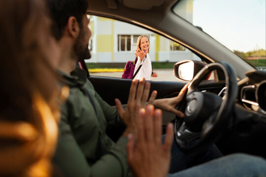 Parents bringing their daughter to school, sitting in car and saying bye to child girl, mother and father waving goodbye to kid