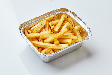 French fries with spices served in an aluminum tray on white background
