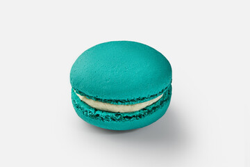Single turquoise macaron with white cream filling on white background
