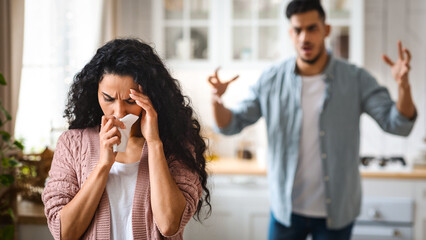 Couple Conflicts. Depressed Arab Woman Crying In Kitchen While Arguing With Husband, Modern Muslim Family Suffering Relationship Crisis At Home, Angry Man Shouting To Wife With Rage, Selective Focus