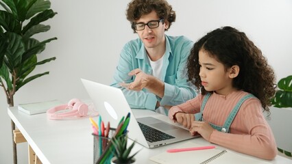 Naklejka premium Caucasian father help student doing homework about engineering code while happy school girl. Dad take care cute child while teaching about generative AI at table with laptop and headphone. Pedagogy.