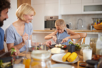 Family enjoys a wholesome meal at home, with a young girl focused on her plate while her parents...