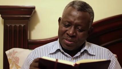 A thoughtful senior African American man smiling while writing his thoughts in a personal journal in his bedroom