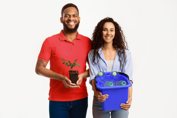 Diverse Man And Woman Holding Green Plant And Plastic Bottles In Garbage Bucket Posing Smiling To...