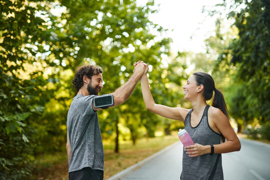 In a vibrant park, two joggers high-five each other, showcasing their accomplishment after a workout in the warm sunlight, emphasizing a healthy lifestyle and camaraderie.