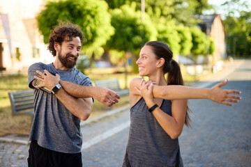 Fototapeta premium Two individuals enjoy a warm afternoon while stretching in a park, fostering a healthy lifestyle and promoting physical fitness. Their smiles reflect camaraderie as they engage in exercise.