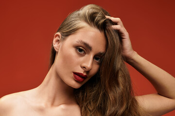 Naklejka premium Captivating young woman poses against a vibrant red backdrop radiating confidence and beauty