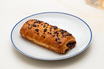 a white plate with a blue ring with a chocolate croissant on a white veined marble background