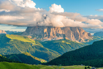 Sassolungo mountain peaks partially covered by dramatic clouds above lush green alpine valley in Italian Dolomites Alps, Alpe di Siusi, Trentino Alto Adige, Italy. Alpine meadow of Seiser Alm