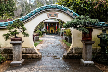 A traditional moon gate leads into a peaceful Chinese courtyard adorned with bonsai trees and classical architectural elements in Kunming, Yunnan, China
