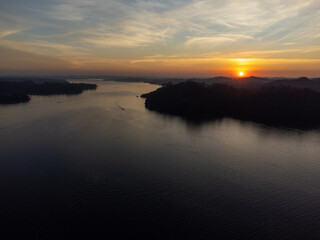 Obraz premium Orange sun setting between mountains behind large lake