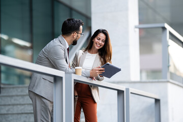 Business colleagues using tablet and having coffee break outside office