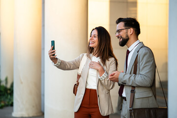 Businesspeople taking selfie outdoors using smartphone smiling and having fun