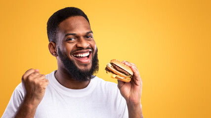 Joyful Black Guy Holding Burger Gesturing Yes Eating Unhealthy Fast Food Standing Over Yellow...