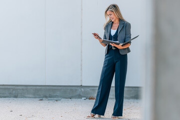 businesswoman with mobile phone and documents outdoors