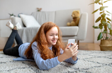 Digital Natives. Portrait of cheerful red-haired teen girl using her smartphone, chatting and...