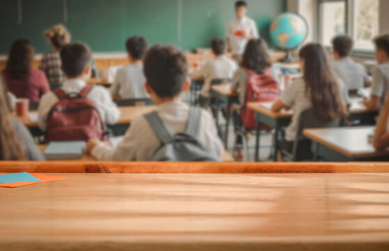 School desk with blurred students and teacher in classroom background. School-related atmosphere of learning, back-to-school excitement, and education in progress.