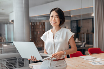 Asian executive manager businesswoman finance analyst using pc for data analysing at workplace. Focused mature eastern business woman working on laptop computer standing in office looking at camera